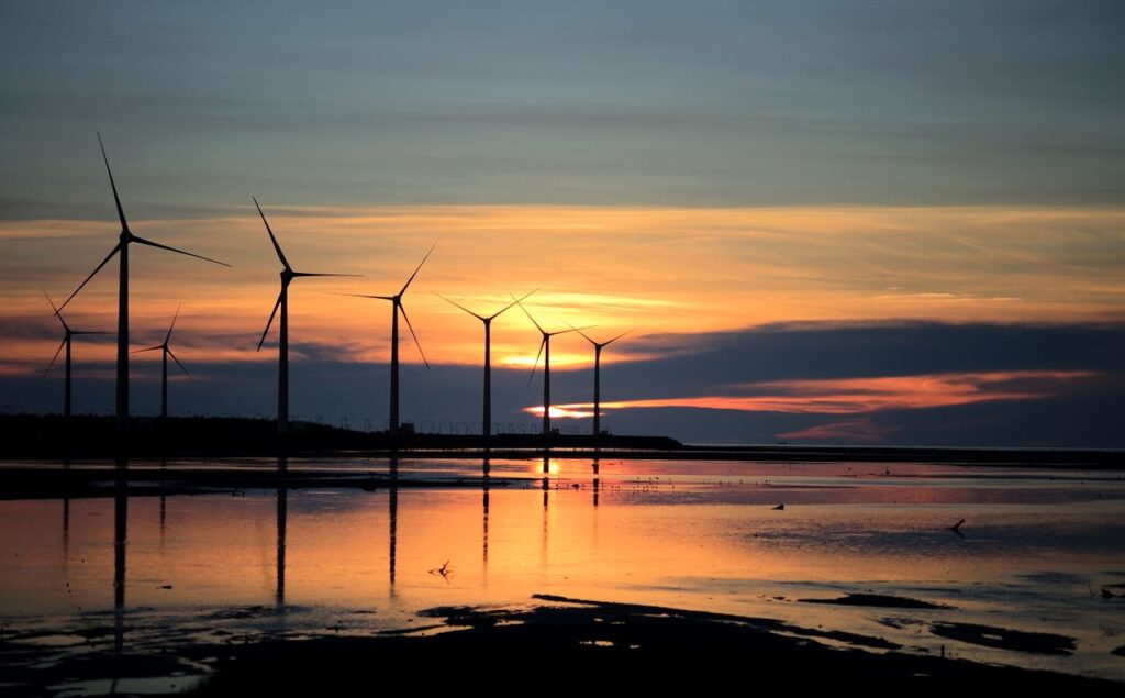 Silhouette of wind turbines during a colorful sunset reflecting on the water.